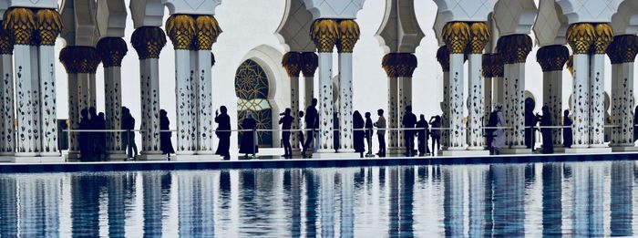 Reflection of people in swimming pool against building