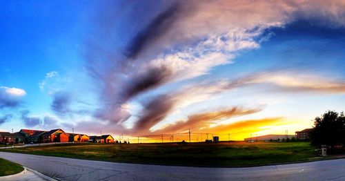 Road by buildings against sky during sunset