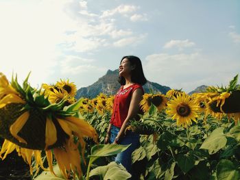 Smiling woman standing by sunflower plants against sky