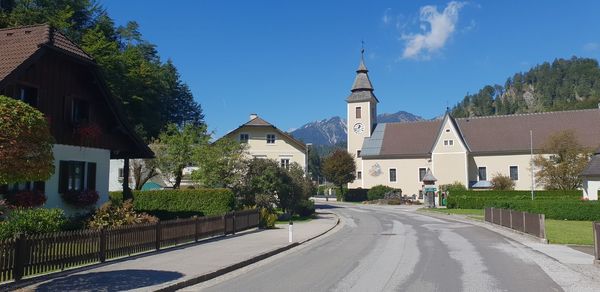 Road amidst buildings against blue sky