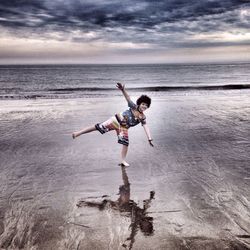 Portrait of playful boy standing on one leg at beach
