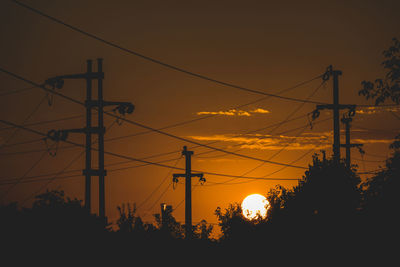 Low angle view of silhouette electricity pylon against sky during sunset