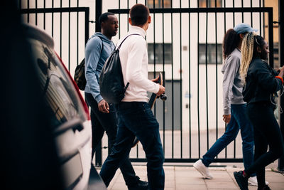 Full length of friends walking on sidewalk by gate in city