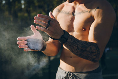 Midsection of shirtless man applying chalk on hand whiles standing outdoors