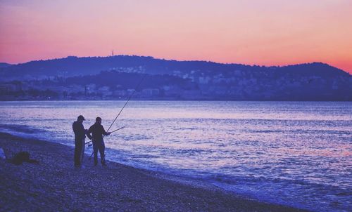 Silhouette man fishing in sea against sunset sky