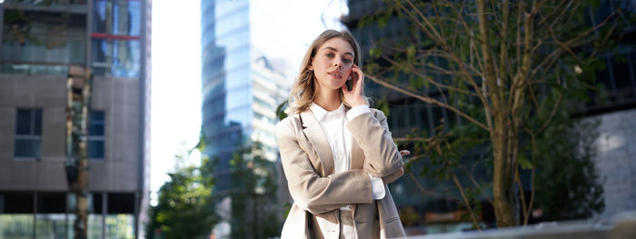 Portrait of young woman standing against building