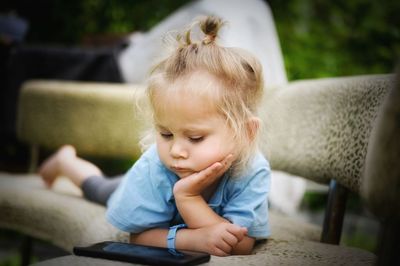 Cute girl looking at mobile phone while lying down on sofa