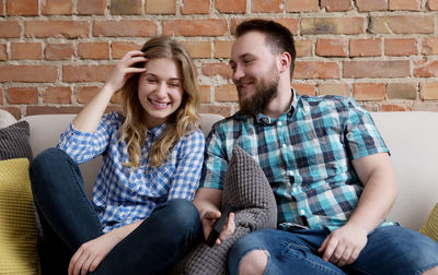 Smiling young couple watching tv while sitting on sofa at home
