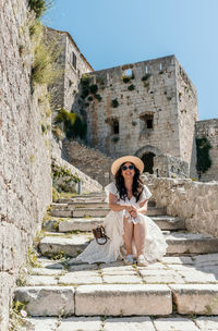 Front view of beautiful woman sitting on stone stairs in medieval fortress klis in split, croatia