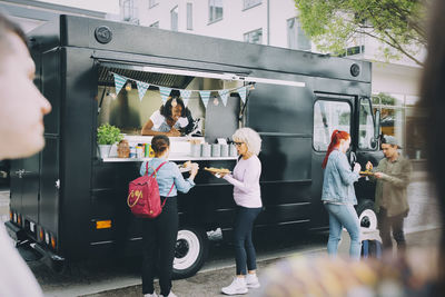 Female owner giving street food to customers while standing in commercial land vehicle