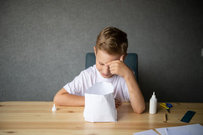 The boy cuts out details from paper. glue the parts together with glue.