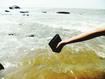 Close-up of hand in sea against sky