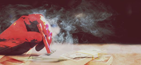 Close-up of hand holding cigarette over paper currency