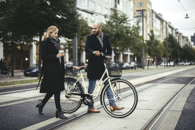 Full length of business people with bicycle crossing city street