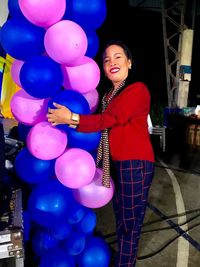 Portrait of smiling young woman holding balloons at night