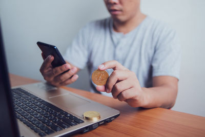 Midsection of man holding mobile phone while sitting on table