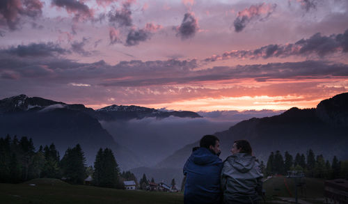 Rear view of young couple sitting against mountain range during sunset