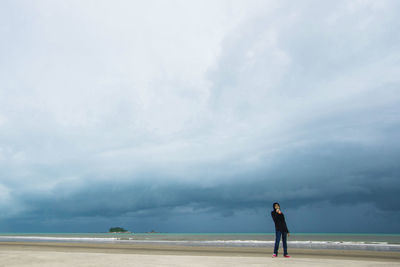 Full length of man standing at beach against cloudy sky