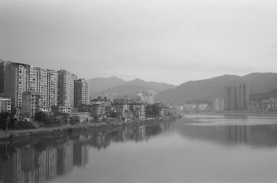 Residential buildings by lake against sky during foggy weather