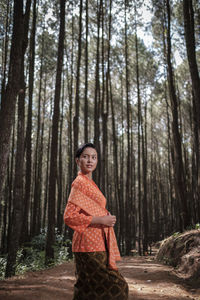 Portrait of woman standing by tree trunk in forest