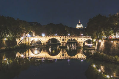 Arch bridge over river in city at night