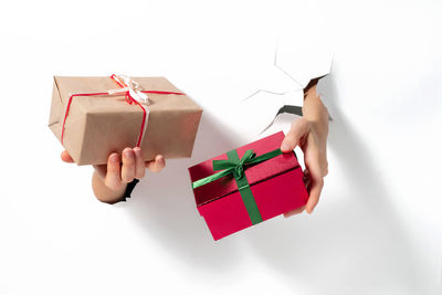 Close-up of female hand holding gift with ribbon through a torn white paper. creative present