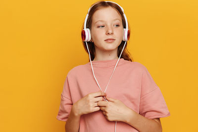 Portrait of young woman holding heart shape against yellow background