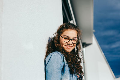 Portrait of smiling young woman standing by wall