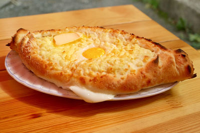 Fresh baked adjaruli khachapuri, traditional georgian cheese and egg bread on wooden table