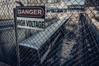 High voltage sign on chainlink fence by train in city