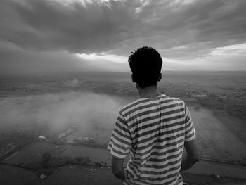 Rear view of man looking at cityscape against sky