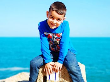 Portrait of happy boy sitting on beach against blue sky