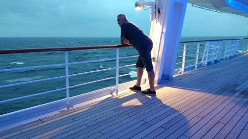 Side view of man standing by railing against sea