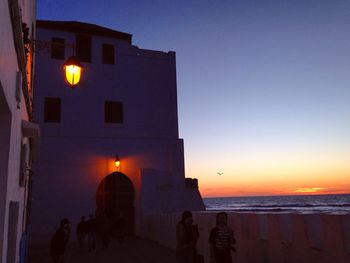 Silhouette building by sea against sky at sunset