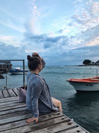 Rear view of woman sitting on pier at sea against sky