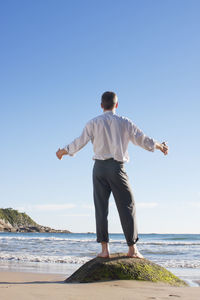 Rear view of man standing on beach against clear sky