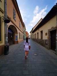 Rear view of woman walking on footpath amidst buildings