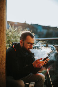 Mid adult man using smart phone while smoking electronic cigarette outdoors