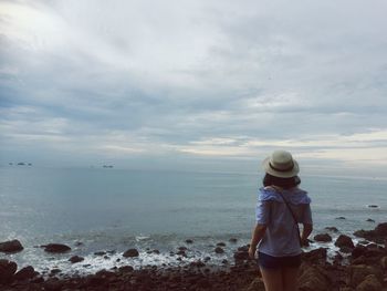 Rear view of woman standing on beach against sky