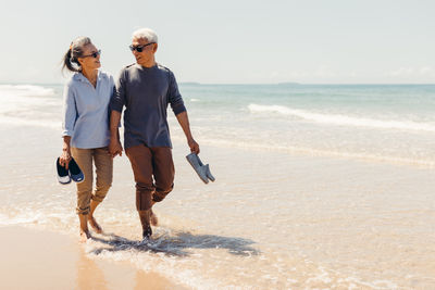 Romantic senior couple strolling happily along the beach in the sunshine and bright sky. 