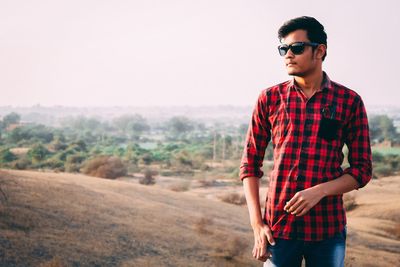 Young man wearing sunglasses standing against sky