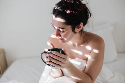 Woman sitting on bed while holding coffee cup at home