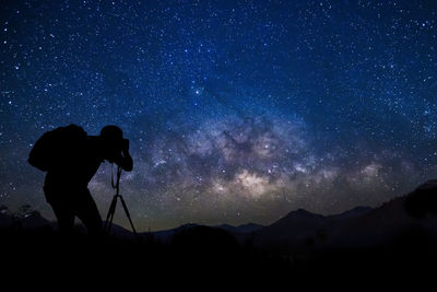 Silhouette man photographing against star field at night