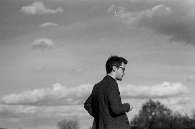 Side view of young man looking away against sky