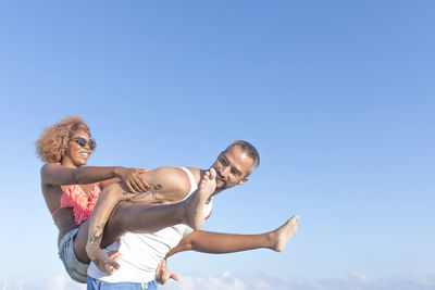Smiling man carrying girlfriend against blue sky
