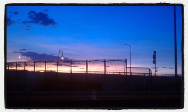 transfer print, sky, auto post production filter, transportation, silhouette, blue, built structure, dusk, railing, architecture, glass - material, outdoors, building exterior, no people, cloud, illuminated, cloud - sky, sunset, window, low angle view