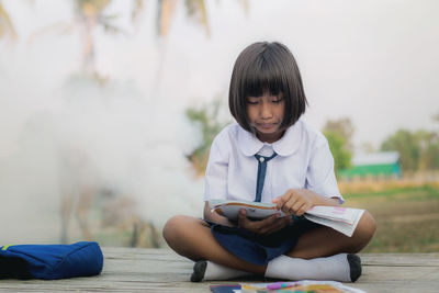 Full length of woman reading book while sitting outdoors