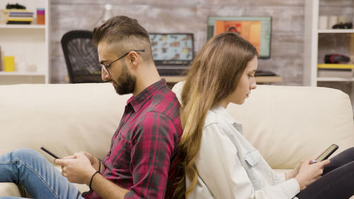 Side view of young woman using mobile phone while sitting at home