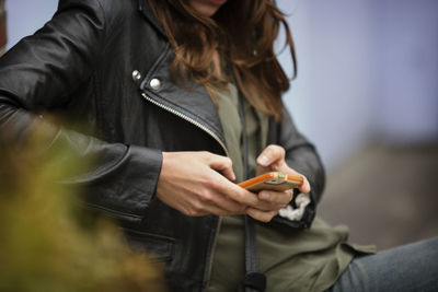 Midsection of woman using mobile phone while resting outdoors