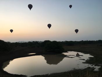 Hot air balloons flying over lake against sky during sunset